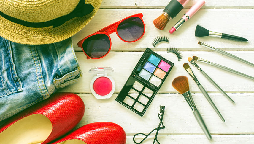 Close-up view of accessories laid out on table including; hat, jeans, shoes, and makeup
